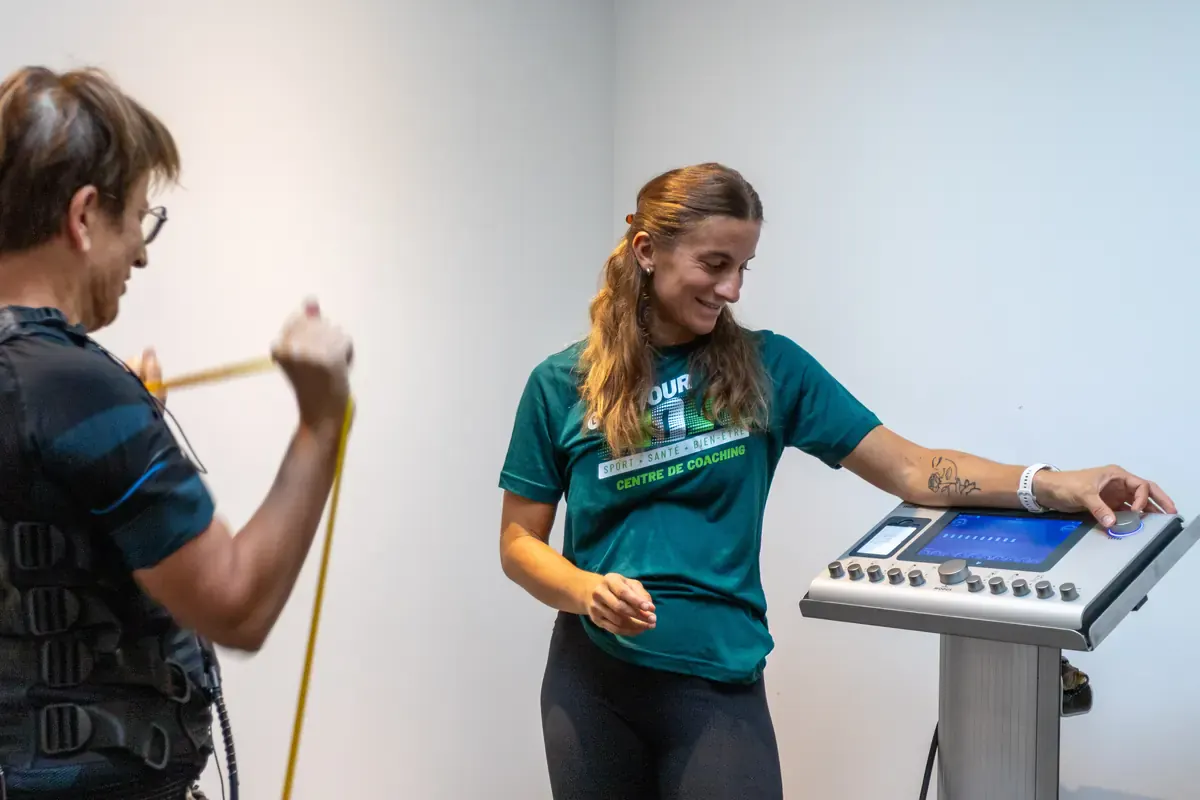 Électrostimulation à Bourgoin-Jallieu : cliente en combinaison EMS accompagnée par une coach devant la machine