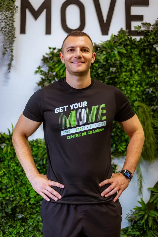 Coach Get Your Move en tee-shirt noir devant le mur végétal au logo du studio