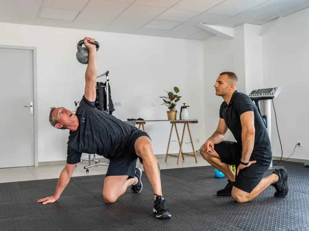 Client au relevé de kettlebell encouragé par son coach Get Your Move
