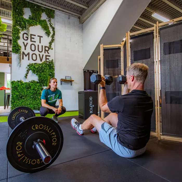 Coaching sportif chez Get Your Move : client au développé haltères suivi par sa coach devant le mur végétal du studio